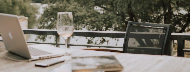 Wine, laptop, and phone on a deck.